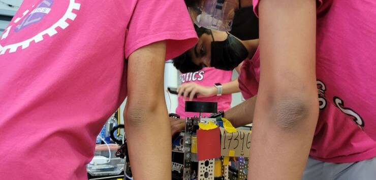 Salem Academy robotics team working together at a tournament wearing pink shirts